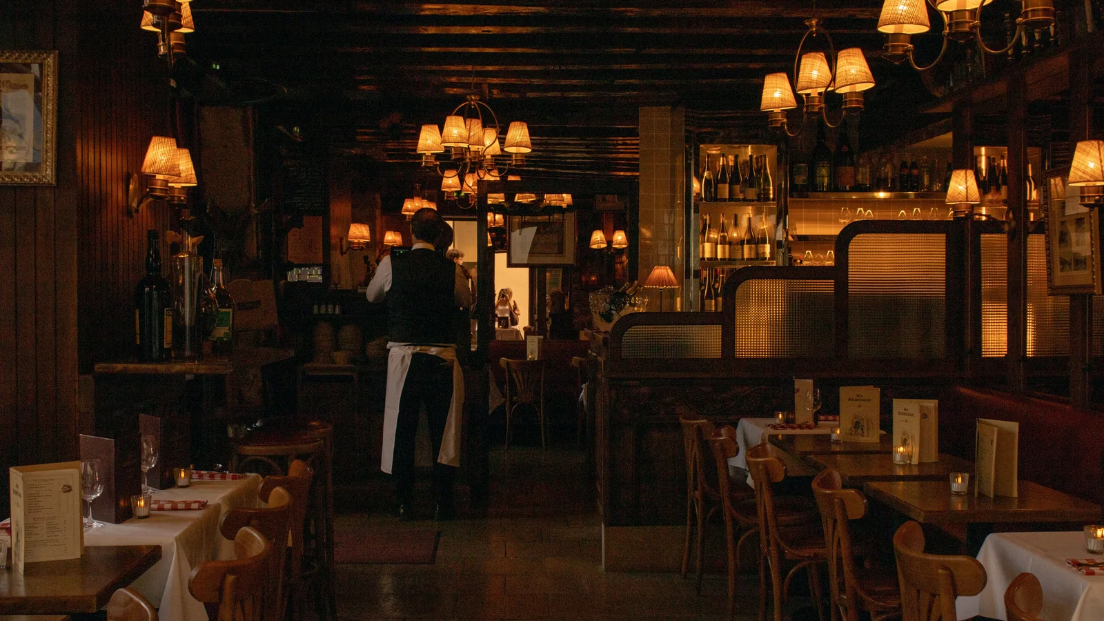 Sfeervol verlicht restaurant met gedekte tafels en een kelner achteraan in de zaal