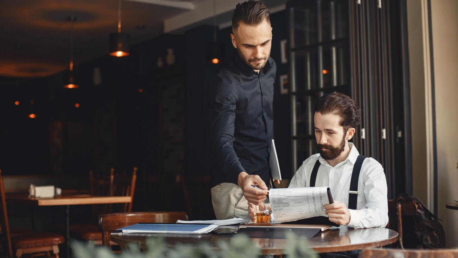 Twee mannen die aan een tafel in een rustig restaurant samen documenten doornemen
