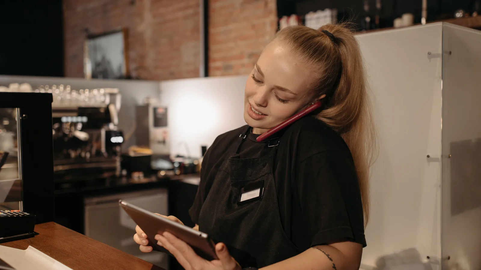 Zaakvoerster aan de telefoon met een tablet in de hand achter de toog