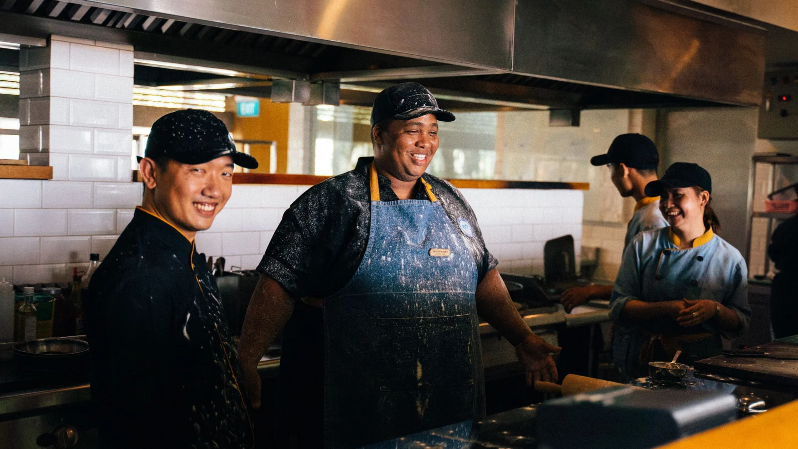Lachende koks met pet en schort samen aan het werk in een restaurantkeuken