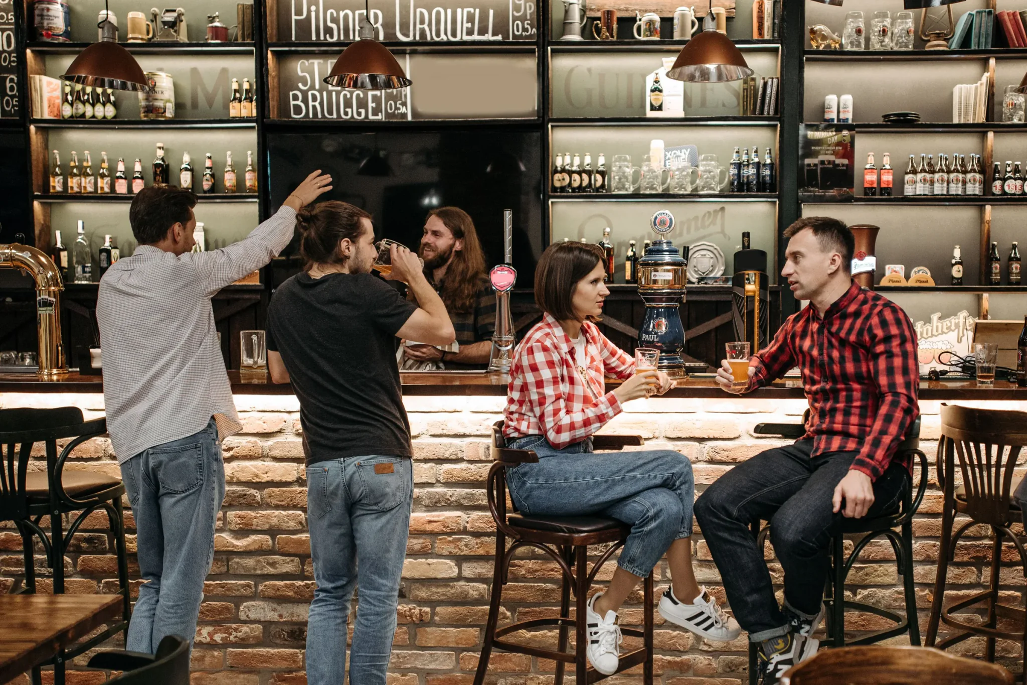 Gasten aan de bar van een druk café, voor een wand vol flessen