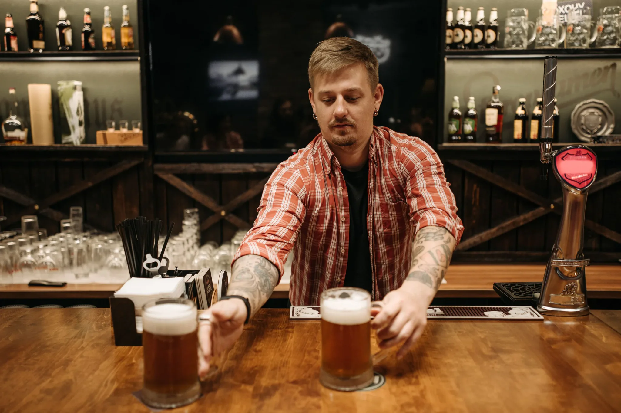 Barman zet twee verse pinten op de houten toog van een café