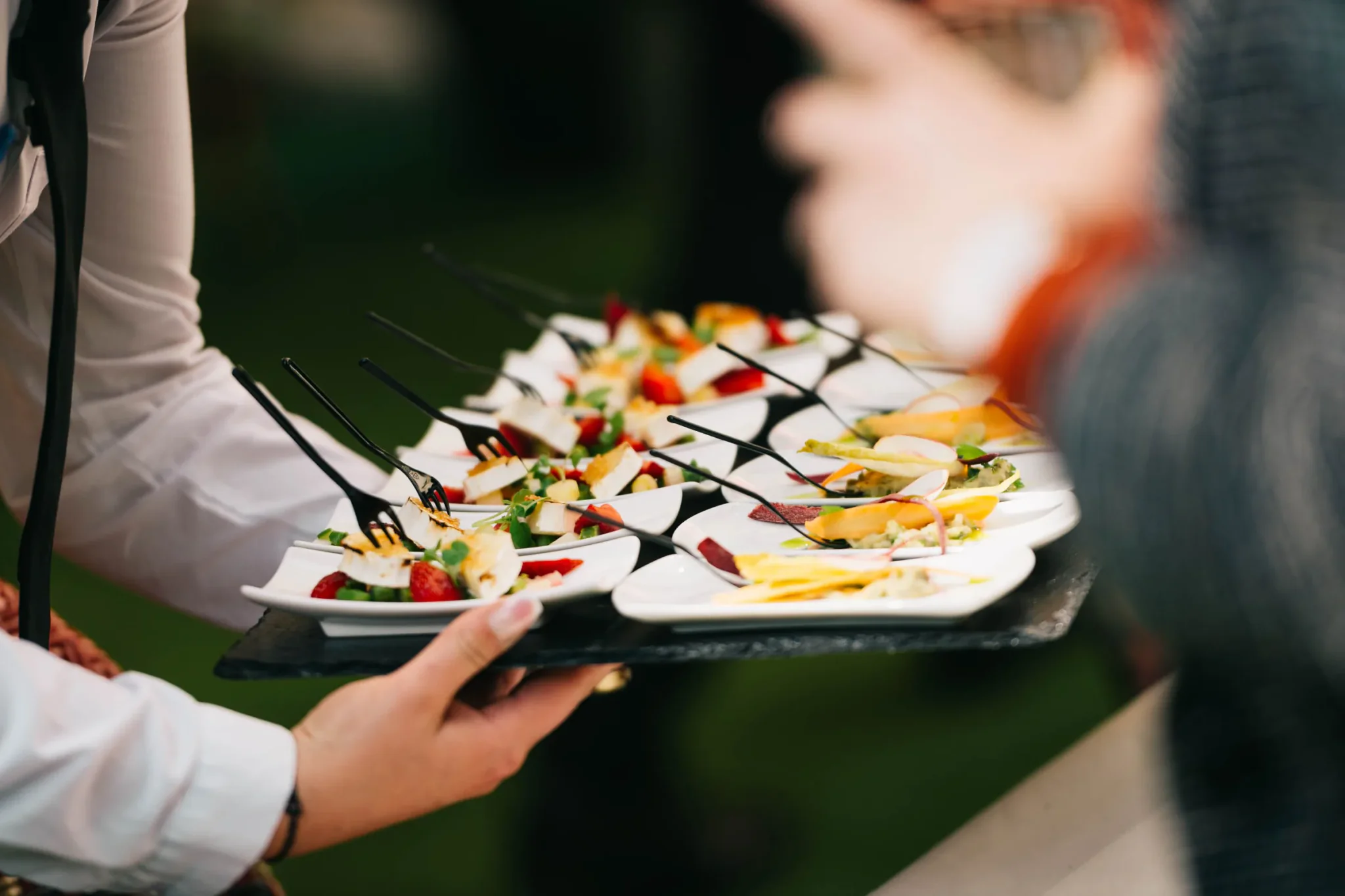 Medewerker draagt een schaal met hapjes rond op een receptie