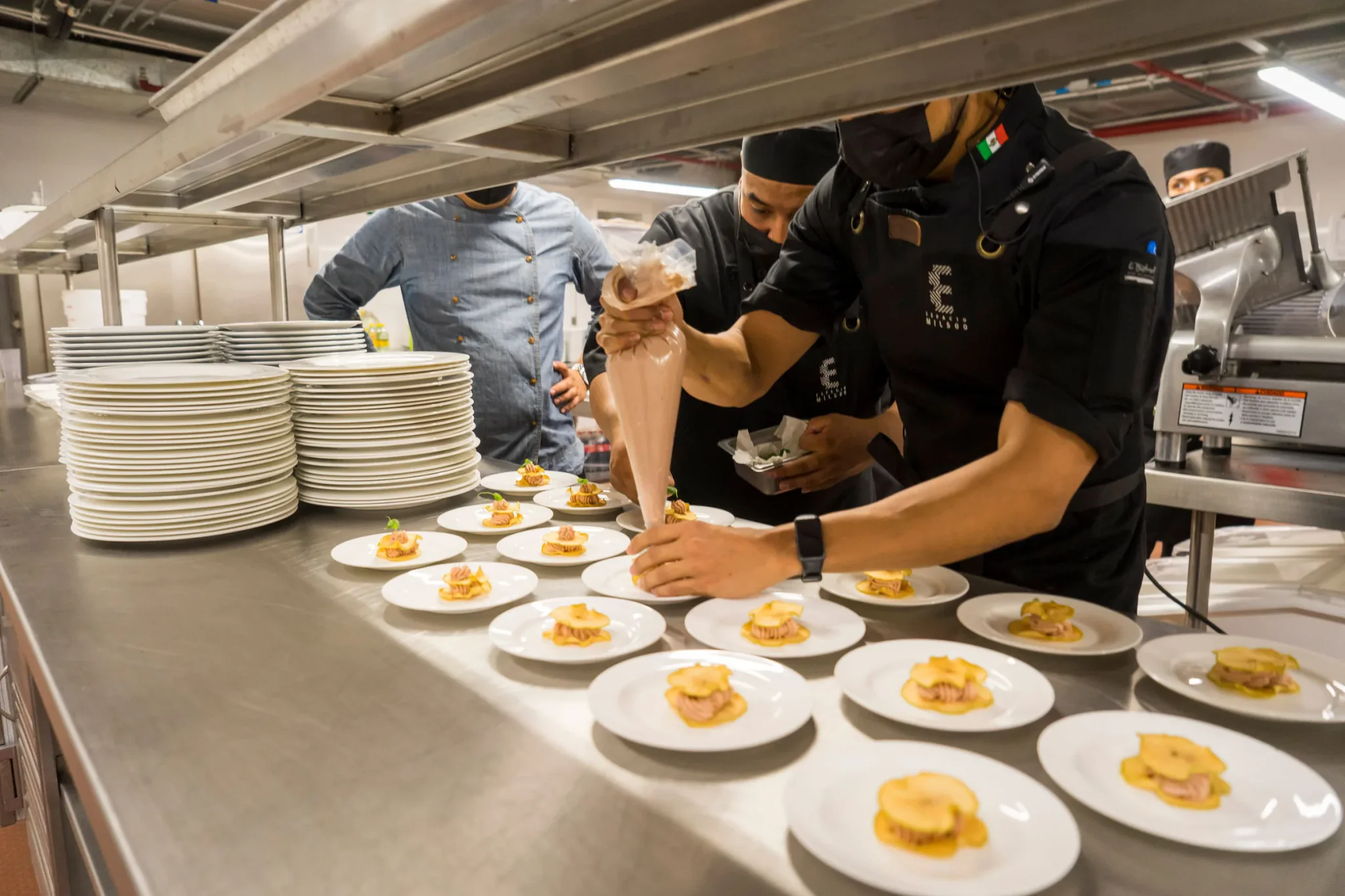 Koks dresseren tientallen borden op een lange inox werktafel in een cateringkeuken
