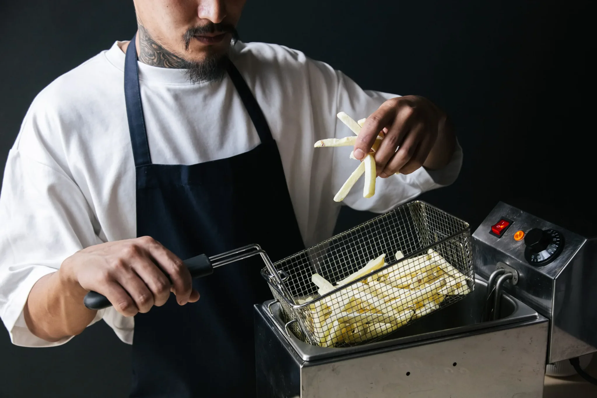 Frituuruitbater laat verse frieten in de frietmand boven de friteuse vallen