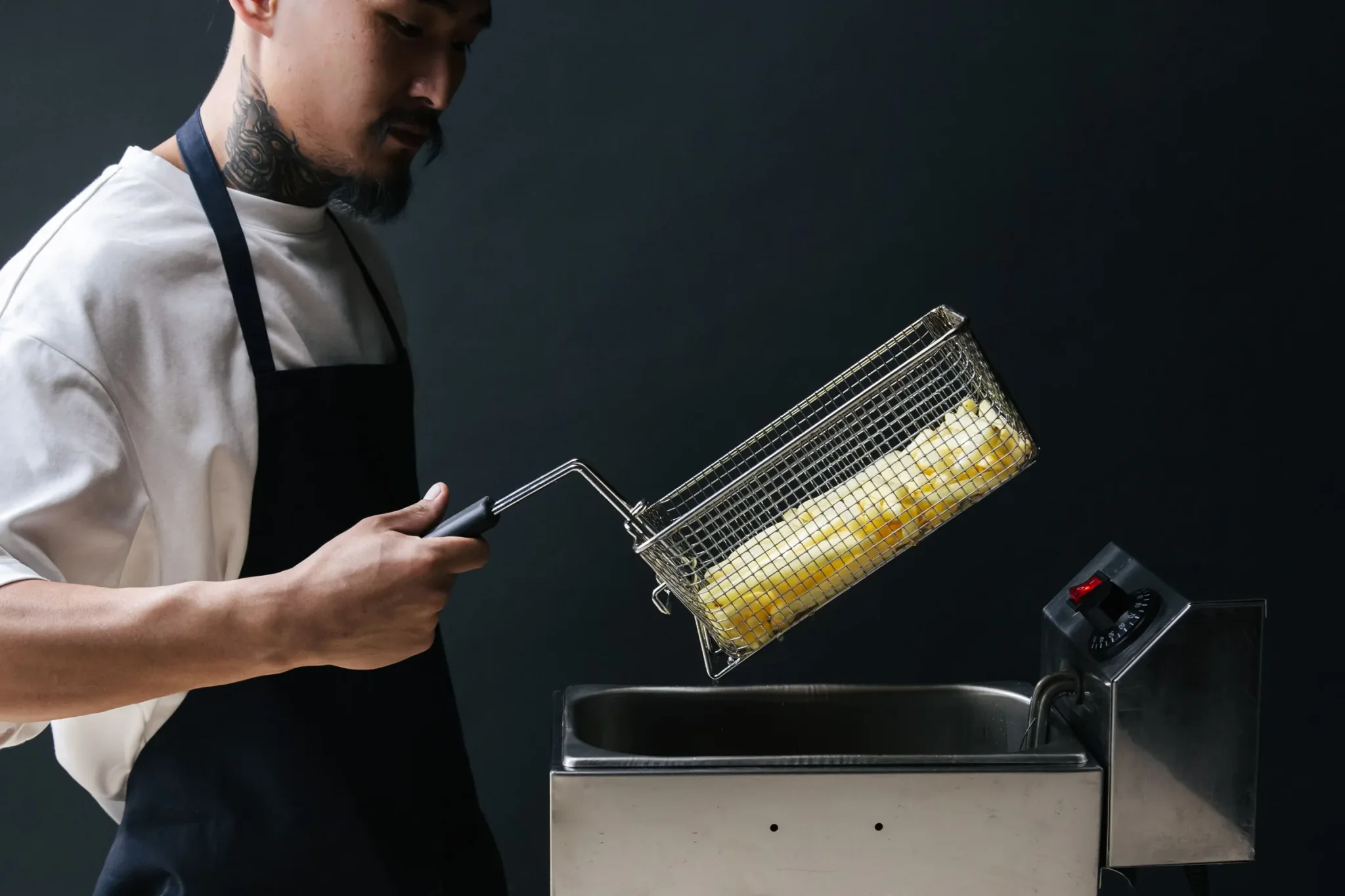 Een frietmand met frieten hangt uit te lekken boven een inox friteuse