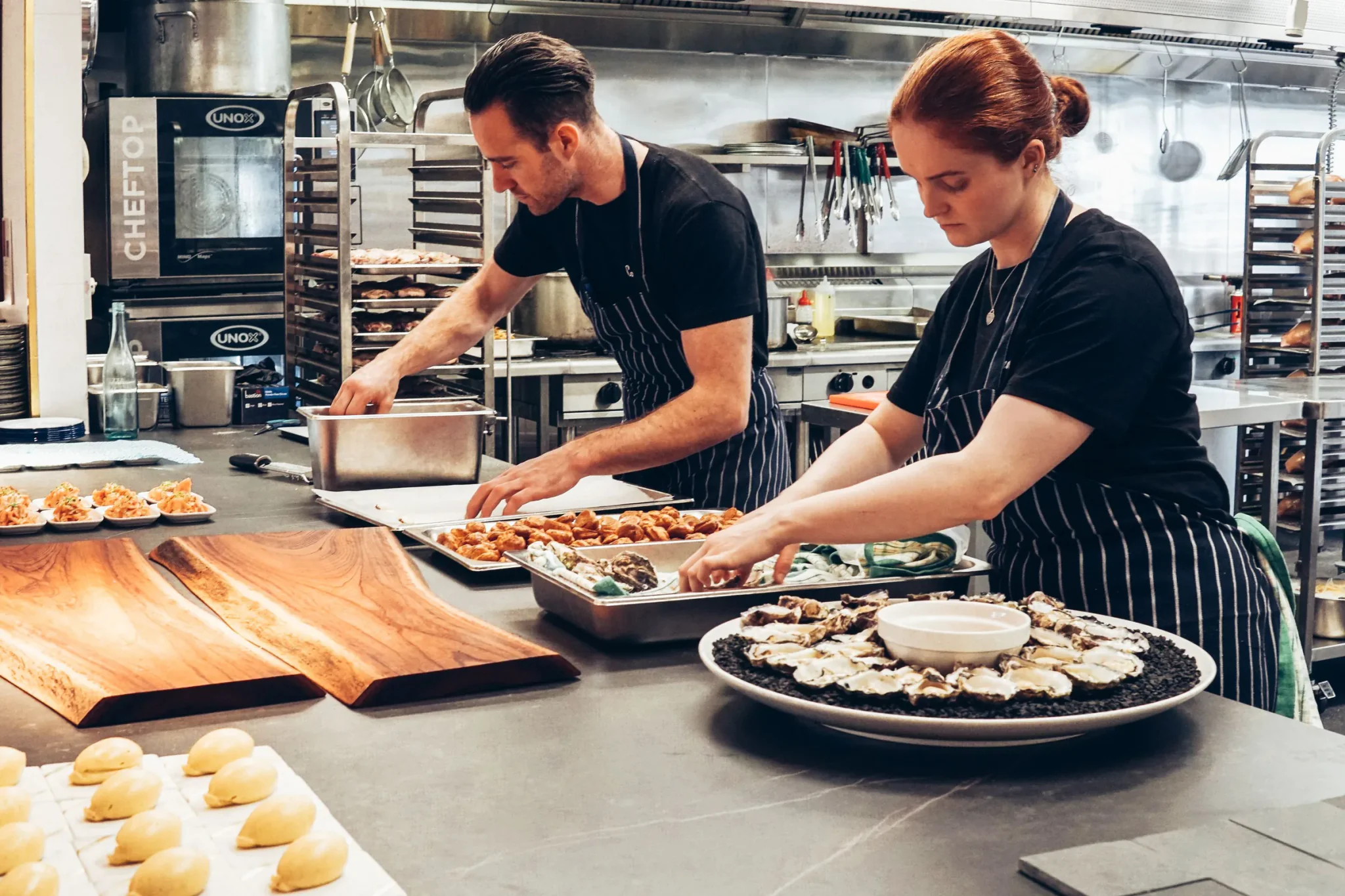 Twee koks bereiden schotels met oesters en hapjes in een open restaurantkeuken
